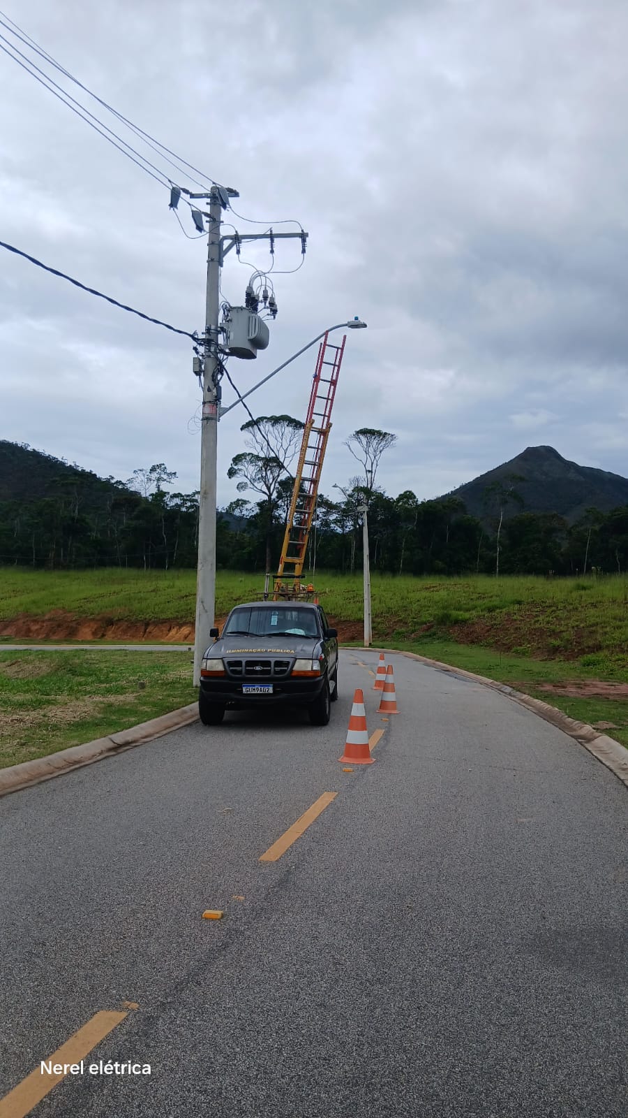 Caminhonete da Nerel Elétrica com escada apoiada em poste durante manutenção de iluminação em via externa